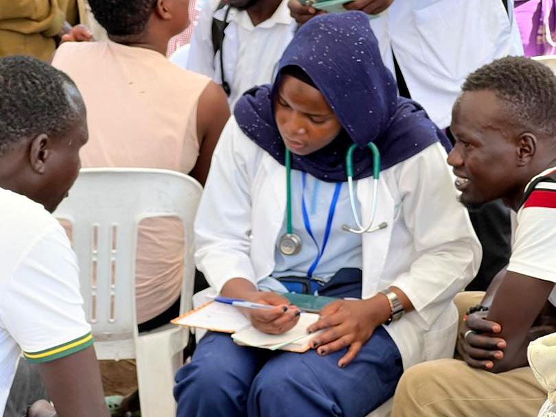 A health worker with a stethoscope takes notes during a consultation